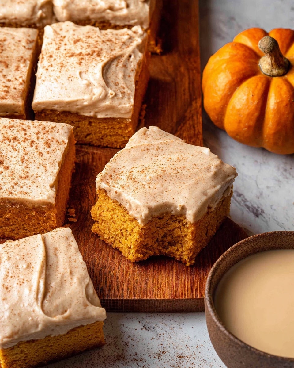 This image shows several square pieces of pumpkin cake with a thick layer of smooth, creamy beige frosting sprinkled with cinnamon on top. One piece is slightly pulled out to show the moist, orange-colored cake inside. The cake pieces are arranged on a wooden surface with a small decorative pumpkin and a round bowl of light beige creamy sauce on the right side. The background is a white marbled texture. photo taken with an iphone --ar 4:5 --v 7