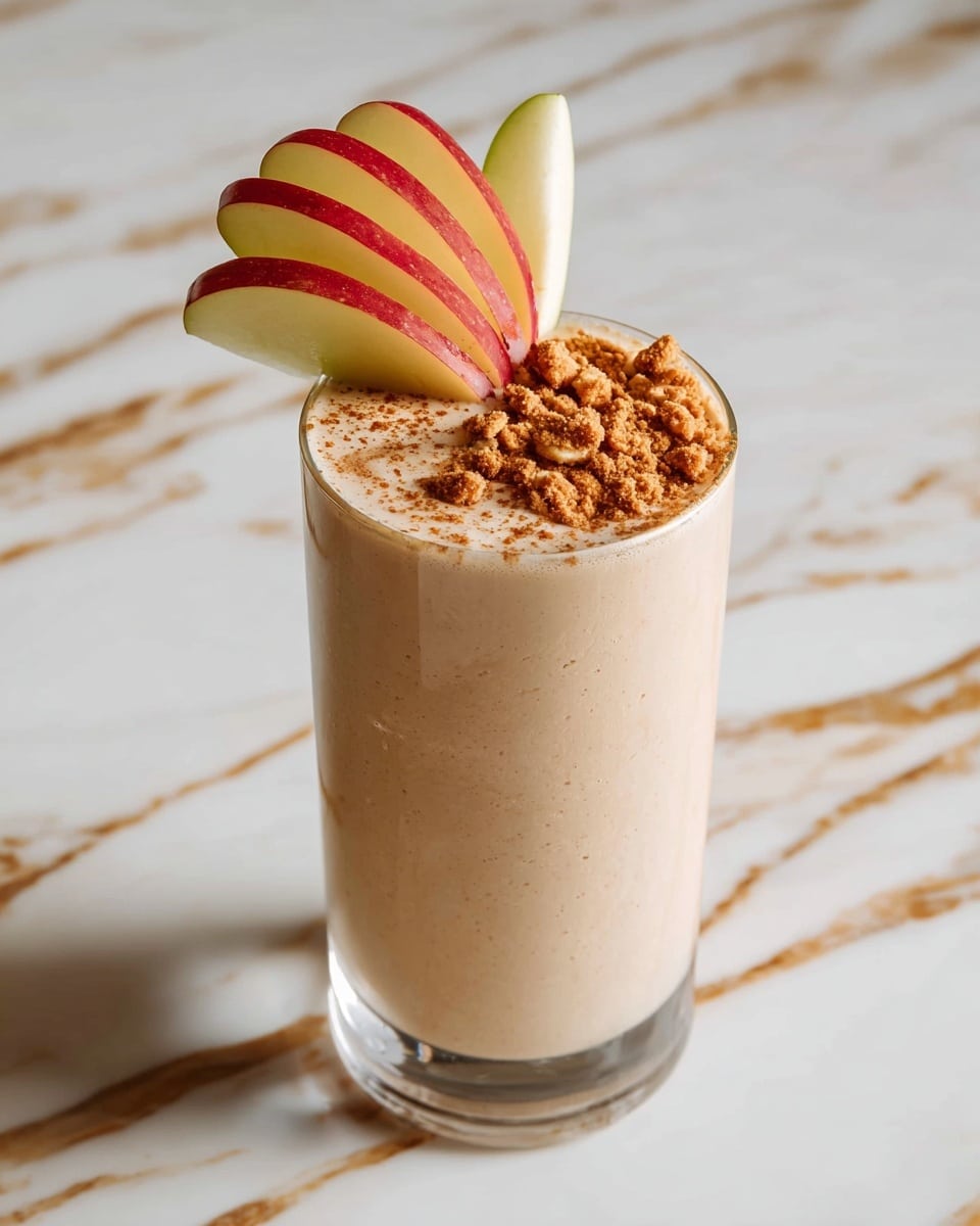 A tall clear glass filled almost to the top with light brown frothy liquid that has a creamy, foamy texture with tiny bubbles and a dusting of cinnamon powder on top; above the glass, a larger clear container is pouring the same light brown, frothy mixture, creating a smooth flowing effect; the setting is a white marbled texture surface with gold veins, giving a clean and bright look photo taken with an iphone --ar 4:5 --v 7