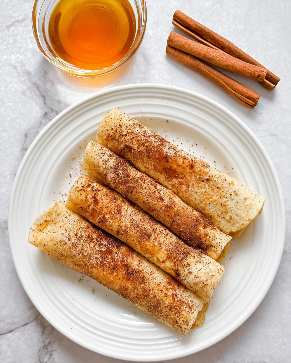 There are three rolled tortillas placed side by side on a white plate with a light ridged edge. Each tortilla is sprinkled with a layer of brown cinnamon and sugar on the outside, giving them a slightly rough texture. The plate sits on a surface with a white marbled texture. To the top left of the plate is a small clear bowl filled with golden honey, and to the top right is a group of whole cinnamon sticks lying together. photo taken with an iphone --ar 4:5 --v 7