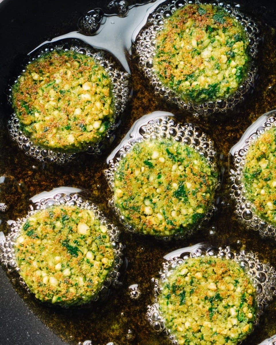 Five round green falafel patties fry in hot oil, each patty showing a rough texture with small chopped herbs and chickpeas visible. The bubbling oil has shiny, round bubbles around each patty, creating a glossy look on the frying surface. The patties are evenly spaced and look fresh and crispy on the edges while still soft inside. The background is a dark frying pan filled with oil over a white marbled surface. photo taken with an iphone --ar 4:5 --v 7