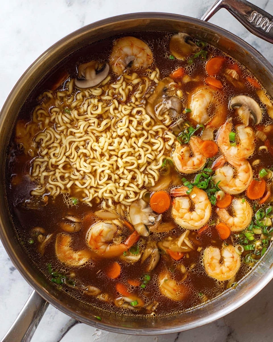 A large stainless steel pot is filled with shrimp ramen soup. Inside, there are two main layers: a nest of curly light yellow ramen noodles placed slightly left of center, and a dark brown broth covering most of the pot. Scattered throughout the broth are pink and white shrimp with orange tails, light brown sliced mushrooms, thin orange carrot strips, and small green chopped scallions. The soup looks warm and well mixed, with some bubbles on the surface. The pot sits on a white marbled surface. Photo taken with an iphone --ar 4:5 --v 7