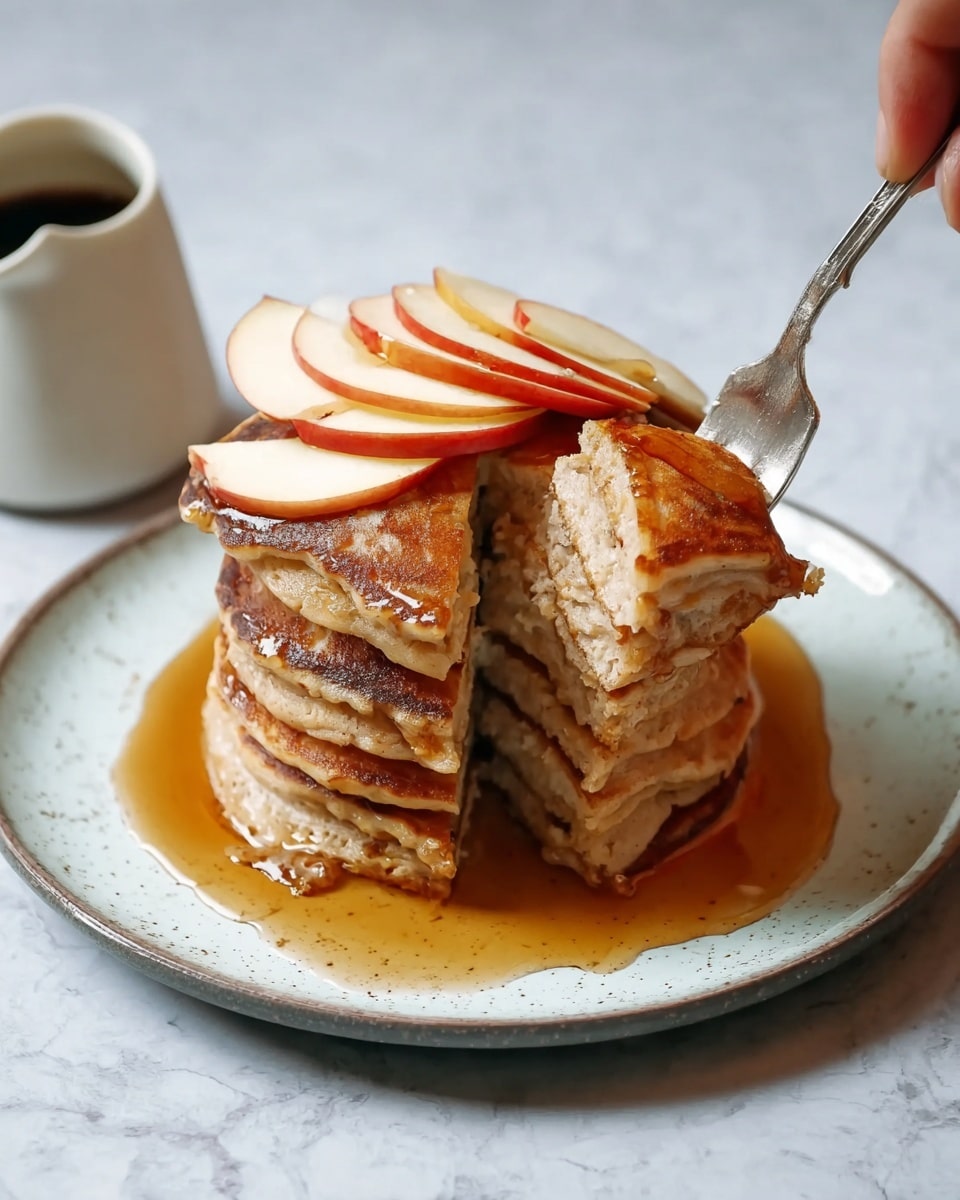 A tall stack of seven golden-brown pancakes sits in the center of a white plate with light blue speckles, each pancake showing a slightly uneven, light crispy edge. On top of the stack, a fan of six thin apple slices with red skin and pale flesh lay neatly. The entire stack is surrounded by a pool of amber syrup that glistens under light. A woman's hand is shown holding a fork, lifting a slice from the side, revealing the soft and fluffy texture inside the pancakes. In the background, on a white marbled surface, there is a small white jug with dark syrup inside. photo taken with an iphone --ar 4:5 --v 7