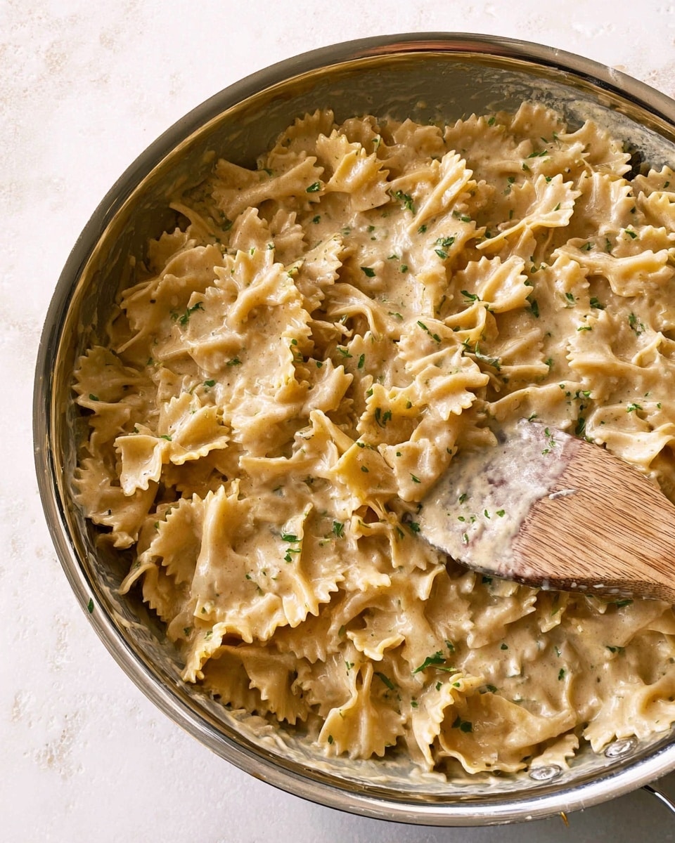 The image shows a bowl of pasta with wide, flat noodles that have ruffled edges, all coated in a creamy sauce with a light beige color. The pasta is topped with small green herb leaves, likely thyme, and sprinkled with black pepper. A silver fork is placed inside the white bowl, which sits on a white marbled surface. The background has a soft, beige cloth with dark stripes, adding a cozy feel to the scene. photo taken with an iphone --ar 4:5 --v 7