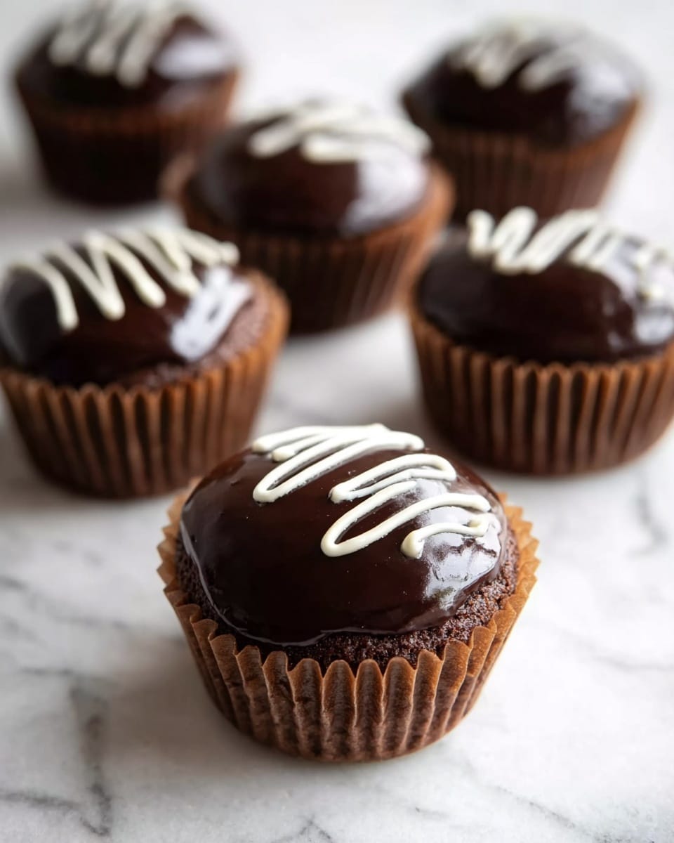 The image shows six round chocolate cupcakes placed on a white marbled surface. Each cupcake sits in a brown paper liner. The top layer of the cupcakes is glossy dark chocolate icing, smooth and shiny. On top of each cupcake's chocolate coating, there is a small squiggle of white icing running down the center, adding a simple decoration. The cupcakes are arranged so that the closest one is in clear focus with the others getting blurrier in the background, creating depth in the image. Photo taken with an iphone --ar 4:5 --v 7