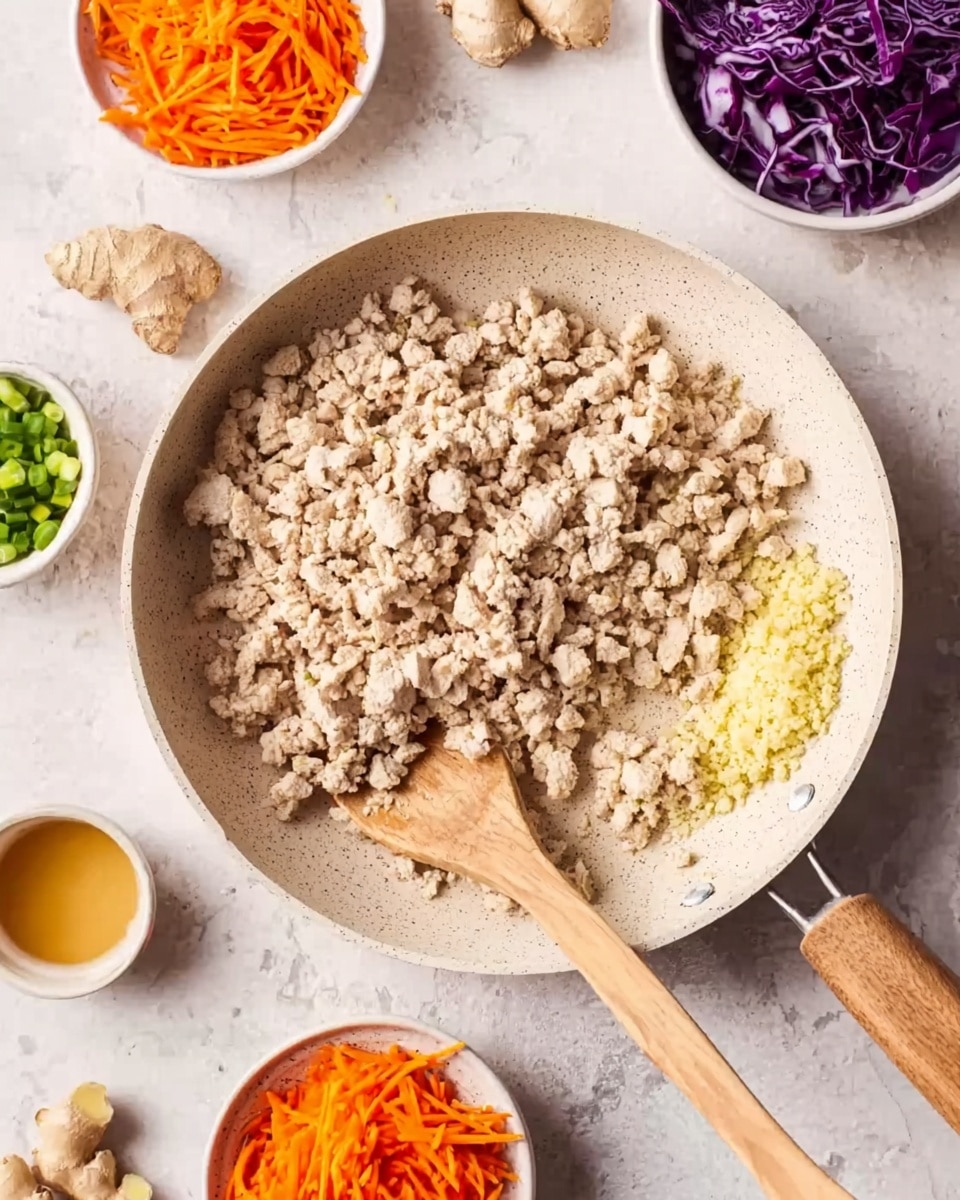 A white pan filled mostly with cooked, light beige ground chicken and a small pile of finely minced light yellow garlic on the right side. A wooden spoon rests on the left side inside the pan. Around the pan, on a white marbled textured surface, there are small white bowls with bright orange shredded carrots, dark purple shredded cabbage, and chopped green onions. Some ginger and ginger slices sit nearby, along with a small amount of golden sauce in a white bowl. A woman's hand is visible stirring the chicken with the wooden spoon. photo taken with an iphone --ar 4:5 --v 7