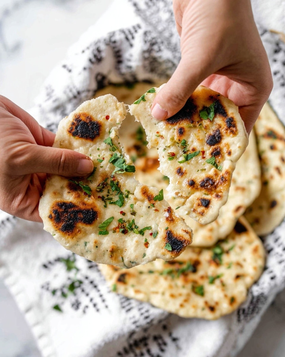 A close-up of two pieces of light beige flatbread with uneven shapes being pulled apart by a woman's hand on each side; the flatbread shows slightly charred dark brown spots and is topped with small chopped green herbs and scattered red chili flakes. In the blurred background, more flatbread is visible on a white cloth with black patterns, all placed on a white marbled surface. Photo taken with an iphone --ar 4:5 --v 7