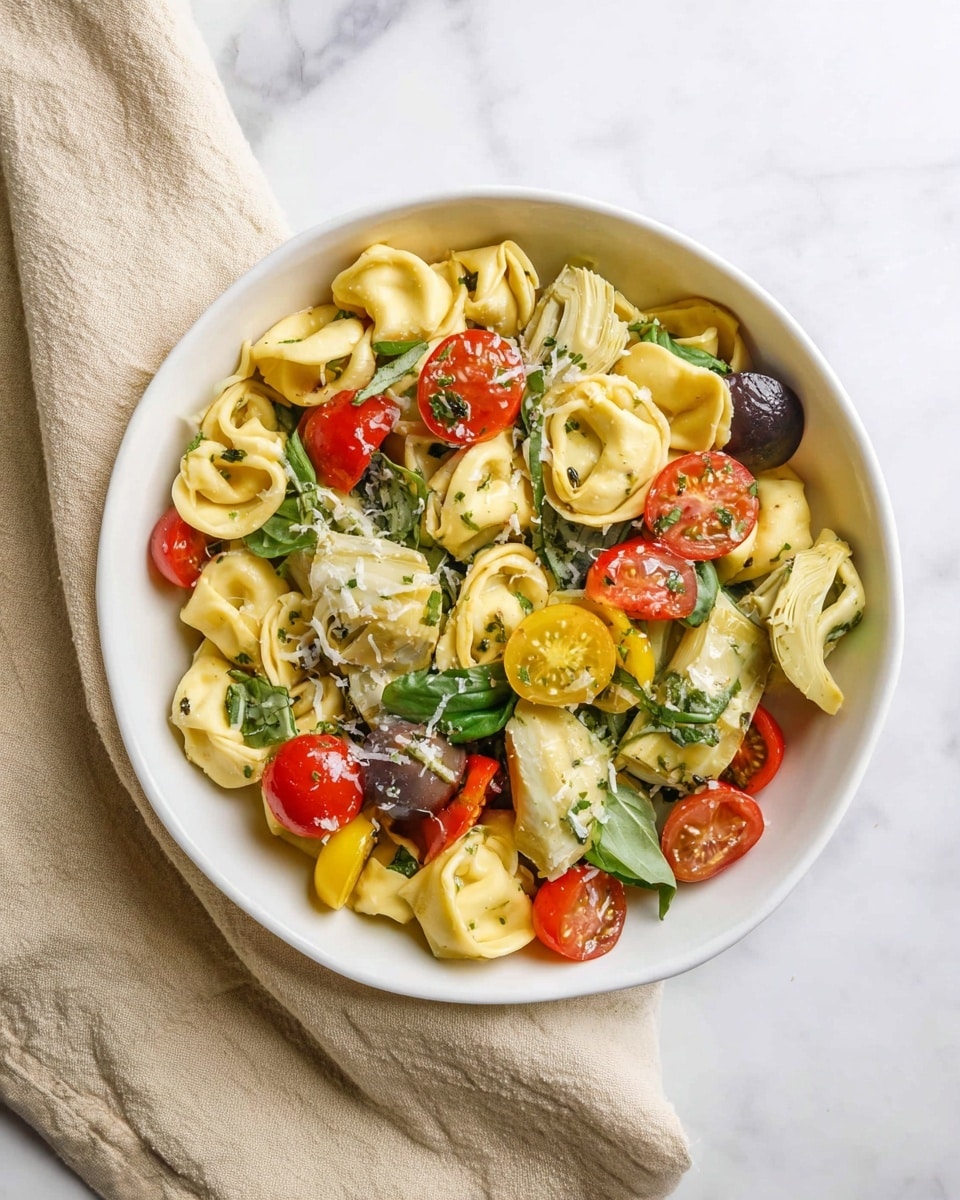 A white bowl filled with three main layers: the bottom layer is light yellow tortellini pasta with a soft, smooth texture; scattered on and mixed with the pasta are pieces of green basil leaves, some torn, adding a fresh look; the top layer contains colorful cherry tomatoes in red, dark purple, and yellow, along with pale green artichoke hearts cut into chunks. The entire dish is sprinkled lightly with shredded cheese and herbs, resting on a white marbled surface with a beige cloth partially visible at the bottom left side. photo taken with an iphone --ar 4:5 --v 7