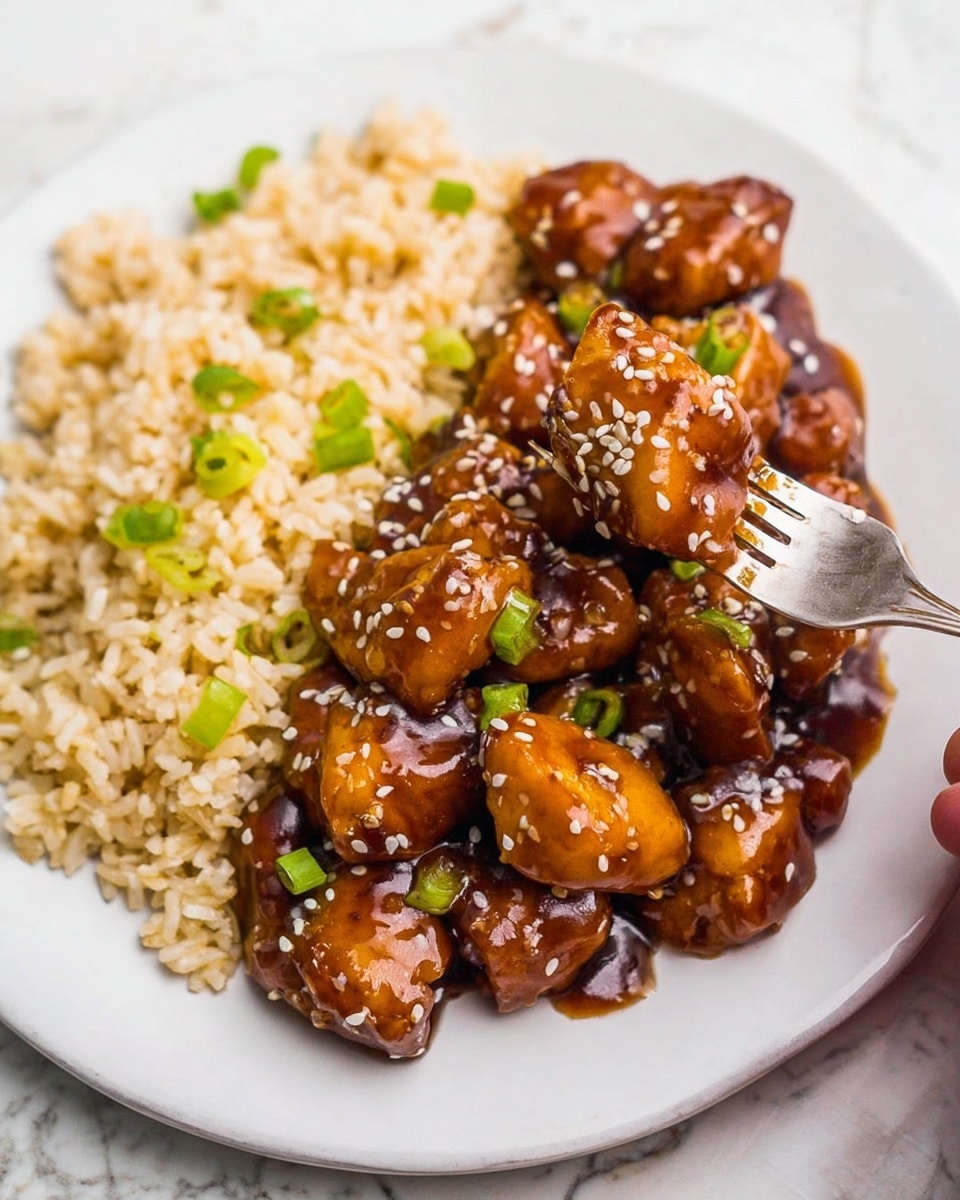 The dish shows a close-up of chunks of glazed chicken in a thick, shiny, dark brown sauce arranged on the right side of a white plate. The chicken pieces are coated and sprinkled with white sesame seeds and small green onion pieces. On the left side of the plate, there is a serving of light brown cooked rice with green onion pieces scattered on top. A woman's hand holding a silver fork with a piece of the chicken is visible in the background on a white marbled surface. The overall colors are warm with a glossy texture on the chicken and a soft texture on the rice. photo taken with an iphone --ar 4:5 --v 7